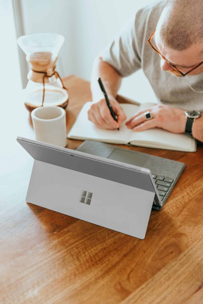 4-Ways-Small-Businesses-Can-Leverage-Microsoft-Copilot-for-SMBs-scaled.jpg a man sitting at a table writing on a notebook