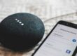 turned-on charcoal Google Home Mini and smartphone